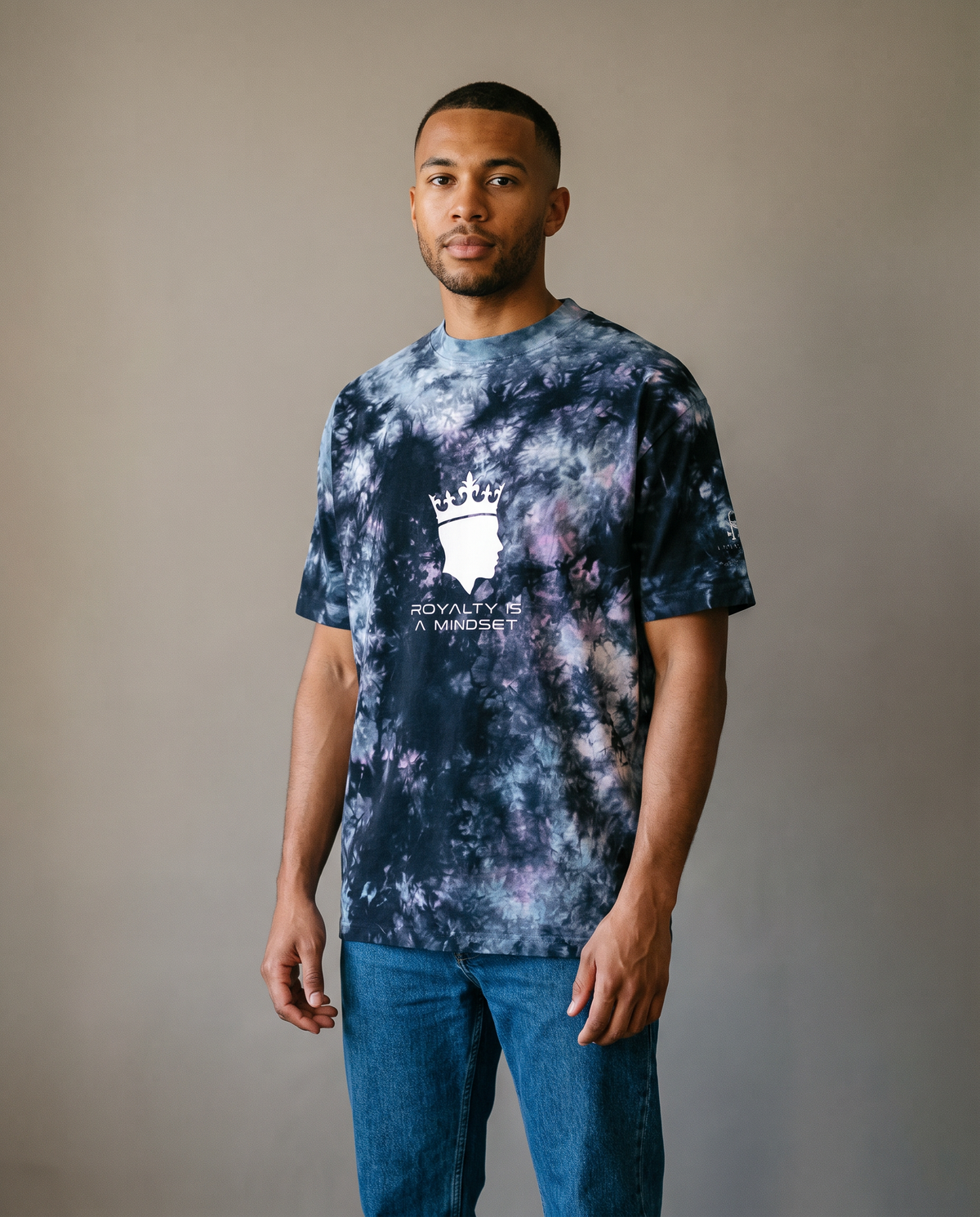 Man wearing the Royalty Is a Mindset tie-dye tee with jeans, studio